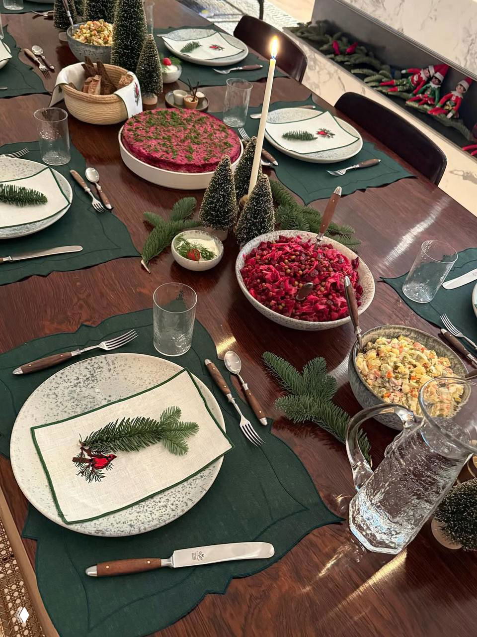 Накрытый стол с новогодней сервировкой: тарелки, салаты, свеча и еловые ветки — домашняя праздничная обстановка.