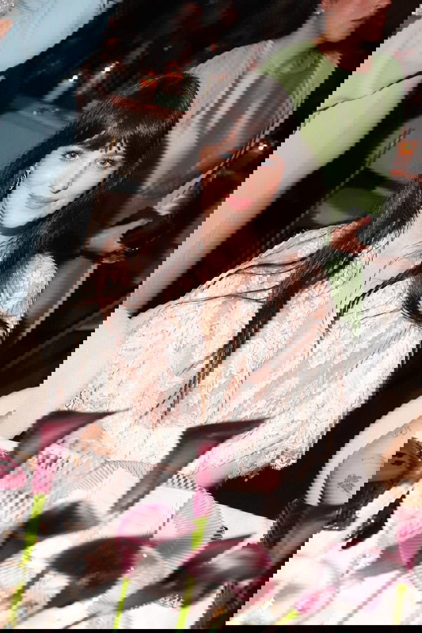 Дакота Джонсон за столом на гала-ужине «Женщины в кино», в кружевном платье Chloé, в кадре элементы сервировки и цветы на переднем плане