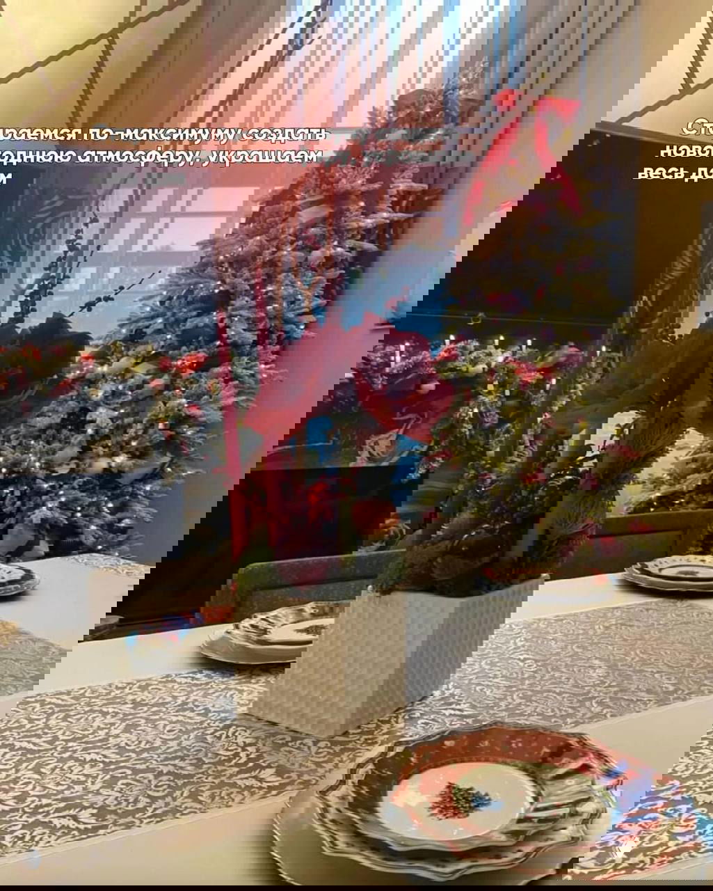 Обеденный стол с рождественской сервировкой и цветочной композицией на фоне украшенной ёлки — детали праздничного интерьера и тарелки с новогодним рисунком.