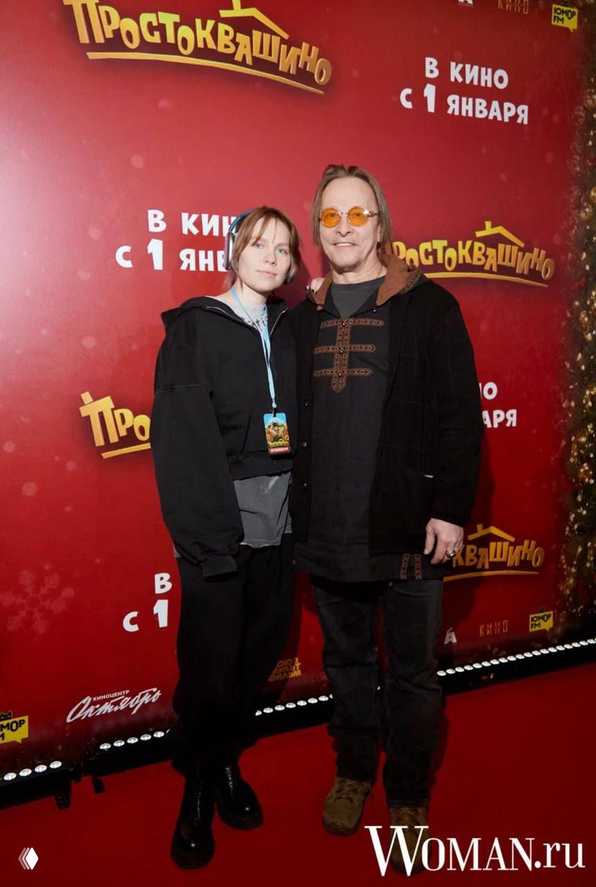 Один из гостей премьеры обнимает дочь на фоне бренд‑стены «Простоквашино» — кадр с красной дорожки семейного показа.