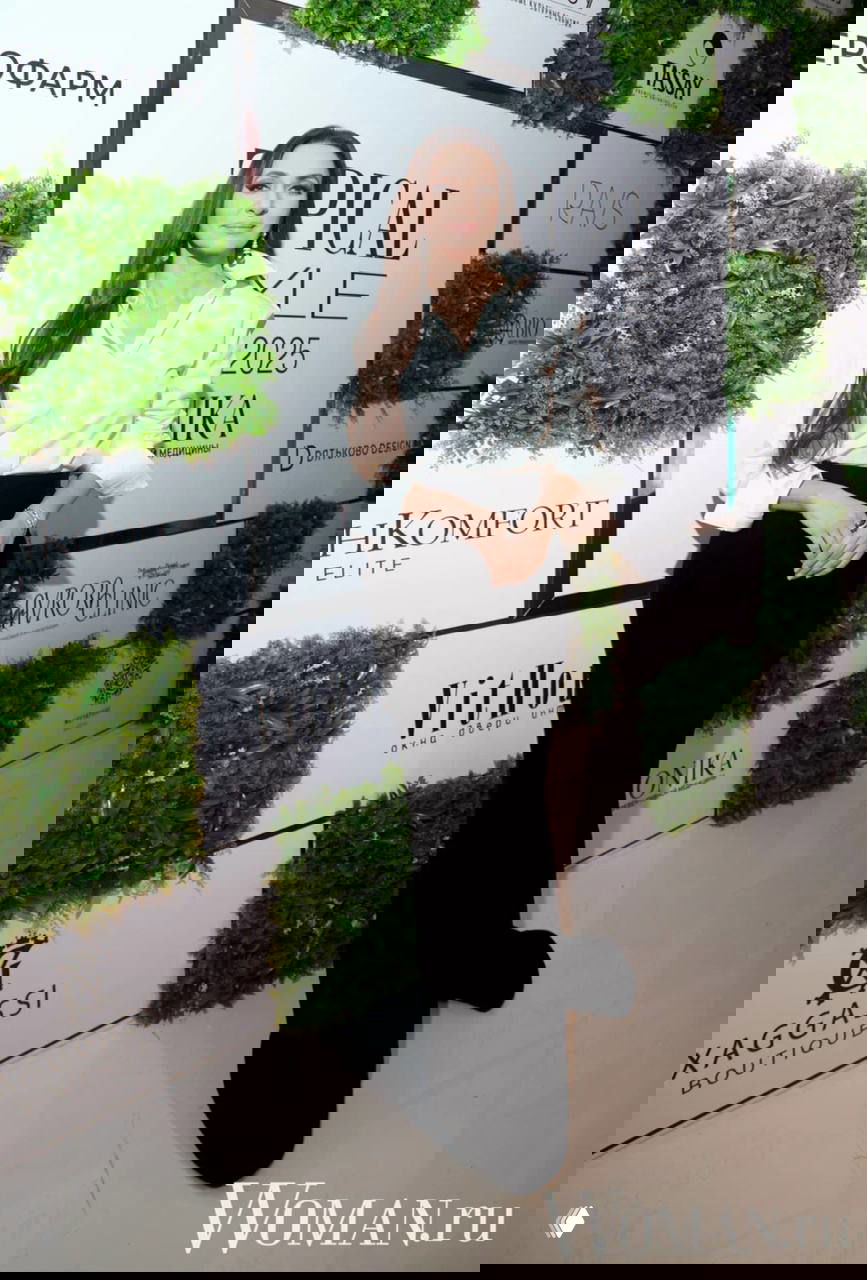 Зара в белой блузе и чёрной длинной юбке на премии Topical Style Awards 2025 на фоне бренд-волла с зелёными панелями и логотипами.