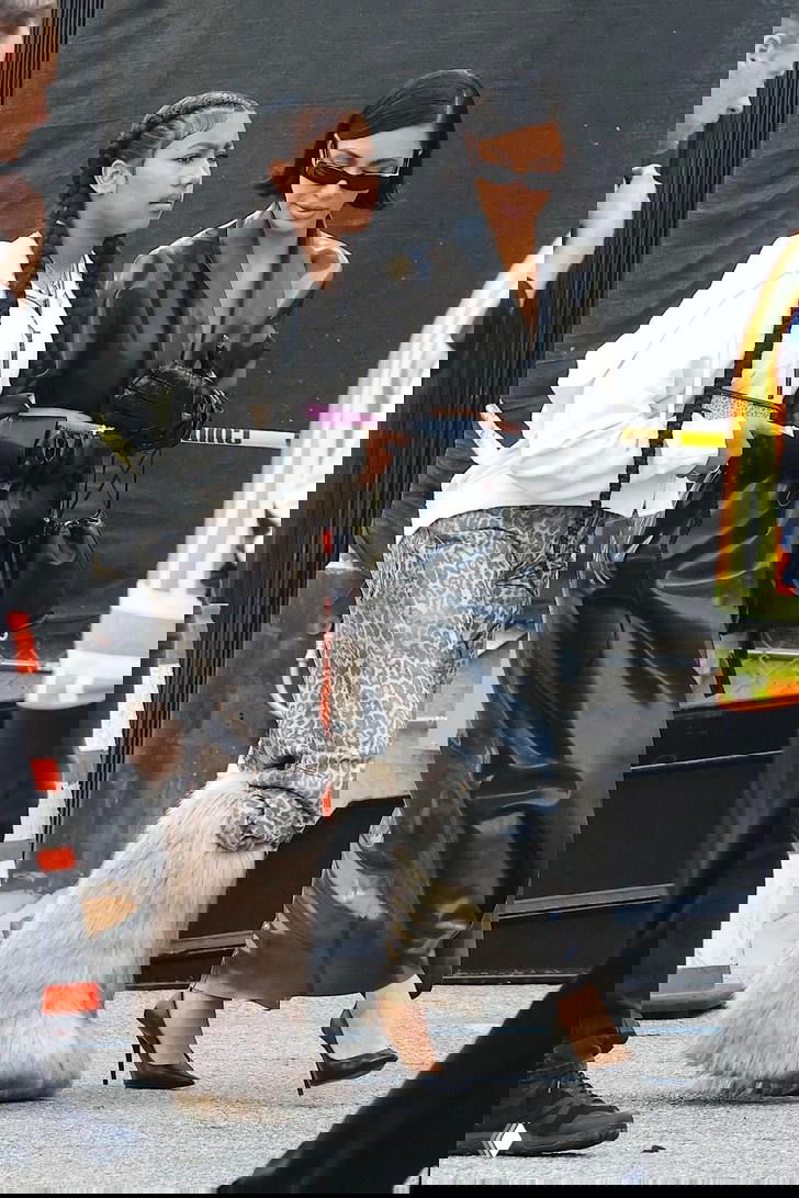 Уличный кадр: подросток в объёмных меховых сапогах и взрослая женщина в лаковой чёрной одежде идут рядом, папарацци-снимок.