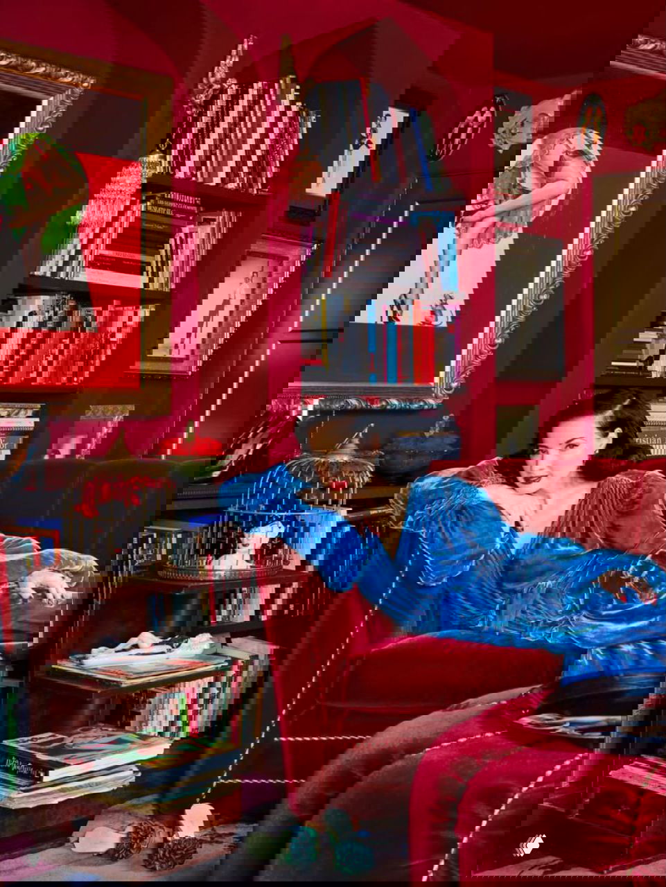 Одна из комнат с насыщенно-красными стенами, книжными полками и Дитой, отдыхающей на бархатном диване в винтажном наряде