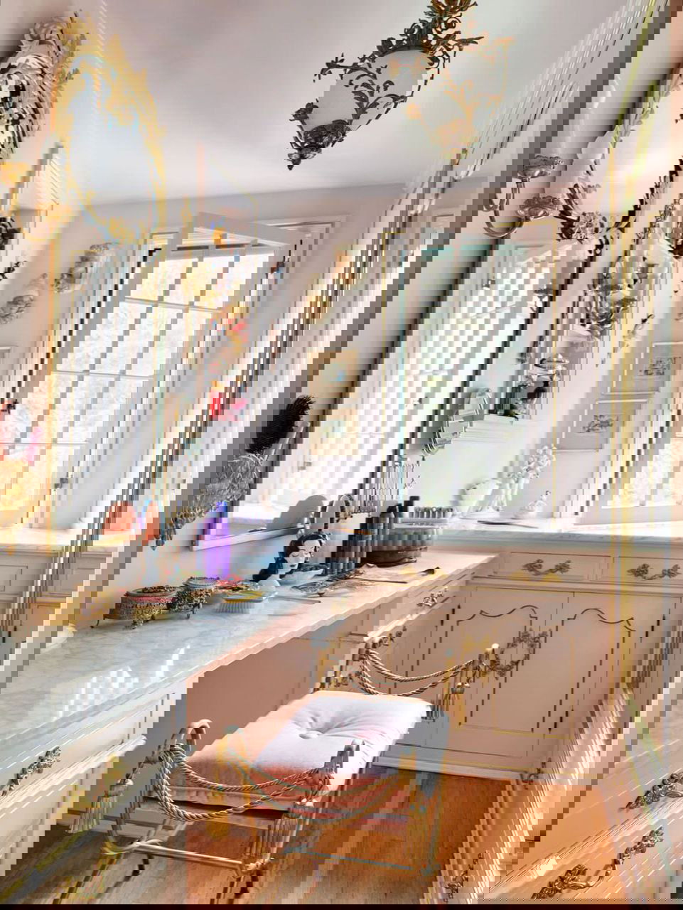 Розовая гримёрная комната с зеркалом, мраморной столешницей и золотыми декоративными элементами в камерном женственном интерьере