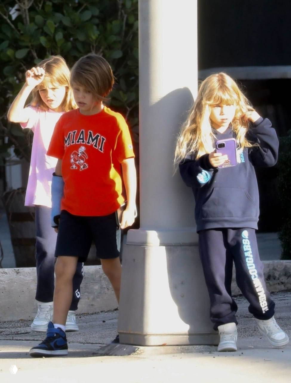 Трое детей Анны Курниковой переходят улицу у опоры: дети в повседневной одежде идут рядом друг с другом после занятий.