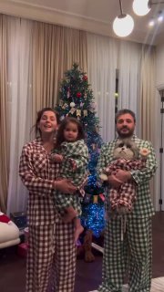 Небольшая семейная сцена в пижамах перед ёлкой: родители и ребёнок держат пушистых питомцев, тёплая домашняя атмосфера праздника.