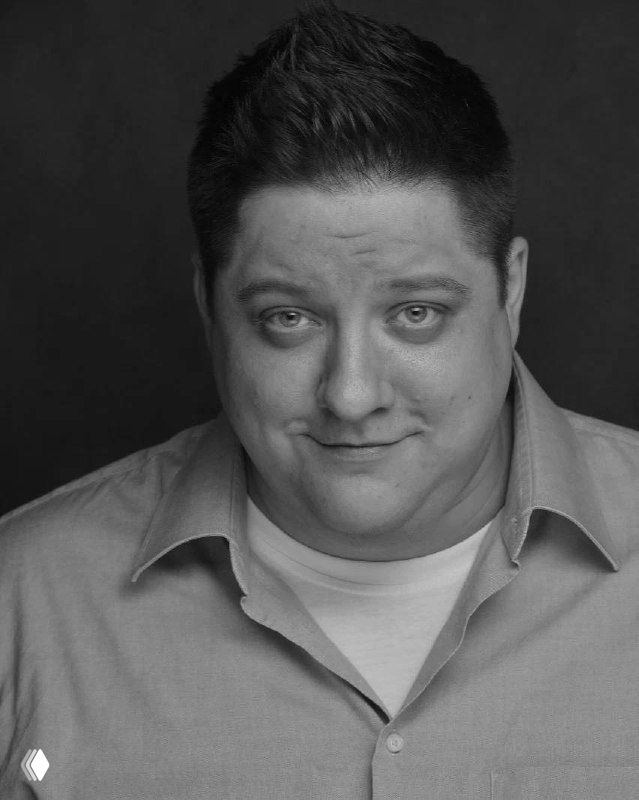 Чёрно‑белый портрет мужчины в крупном плане с заметными цифровыми искажениями изображения, видны лицо и плечи в портретном формате.