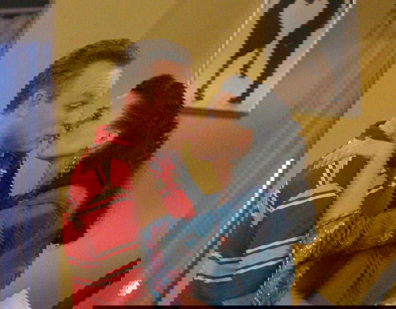 Сцена из комедийной сцены: пара героев целуется на фоне яркого декора, эмоциональный момент из эпизода телесериала в студийной обстановке.