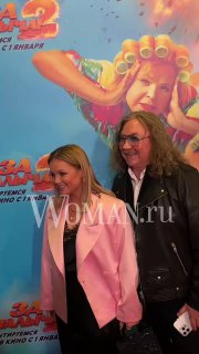 Два человека на красной дорожке у постера фильма: женщина в светлом пиджаке и мужчина в тёмной куртке.