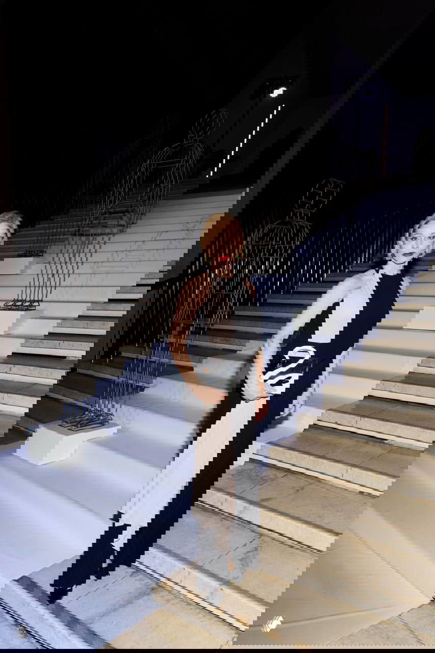 Гостья в двухцветном чёрно‑белом платье стоит на ступенях рядом с декоративными скульптурами, подчёркивая театральную атмосферу вечера Lamoda.