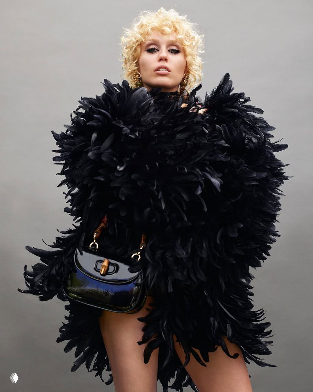 Майли Сайрус в драматичном перьевом чёрном пальто с маленькой сумкой — театральный модный образ для журнальной съёмки.