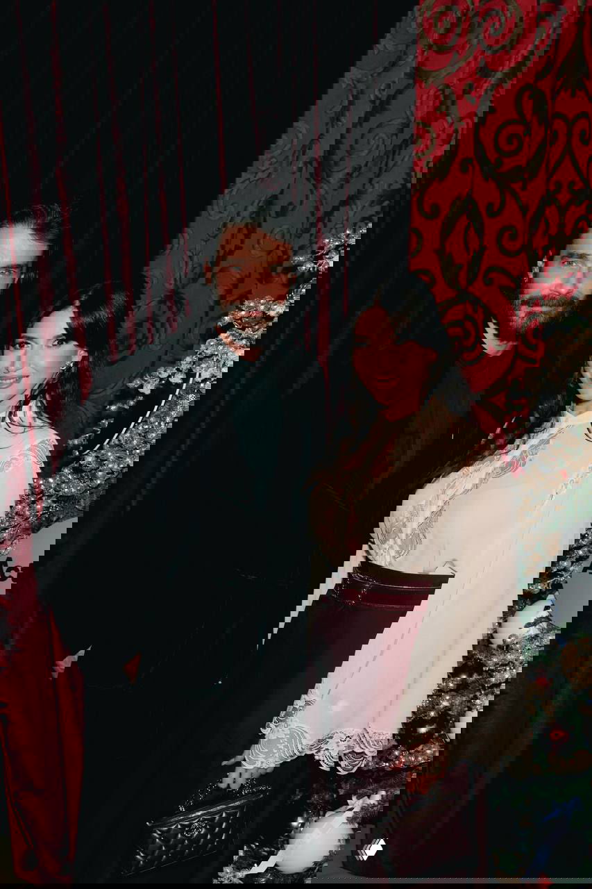 Мужчина и женщина позируют на фоне бархатных красных штор и рождественского декора — фотозона благотворительного вечера ACTION, праздничный антураж.