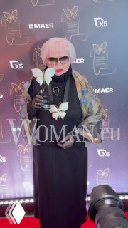 Светлана Крючкова в солнечных очках и тёплом наряде на красной дорожке церемонии «Бриллиантовая бабочка», фон с логотипами.