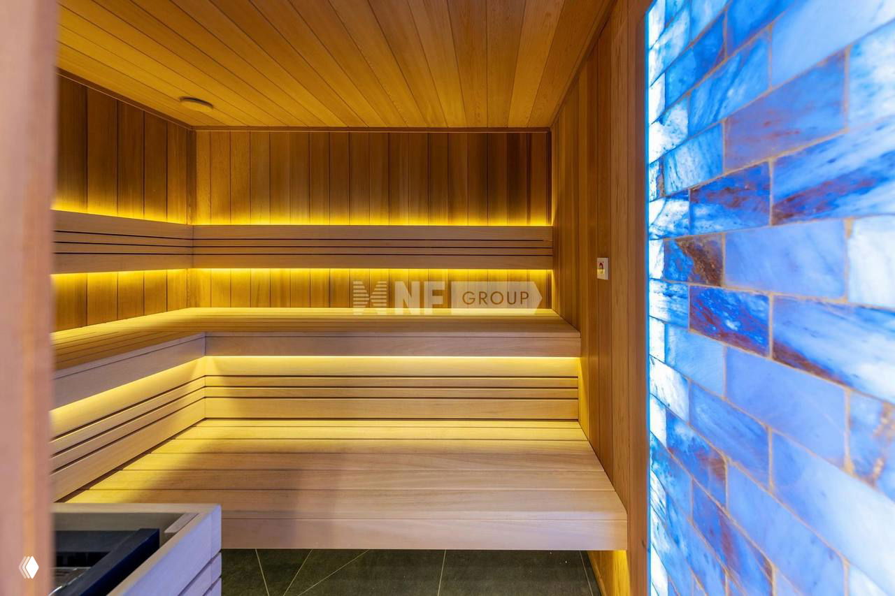 Интерьер бани/сауны с деревянными скамьями, подсветкой и панелями из светлого дерева; современное оформление зоны отдыха на участке.