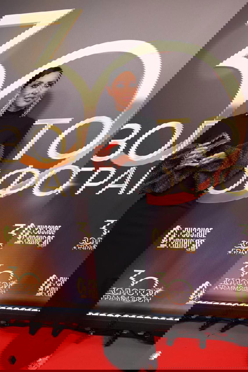 Алсу в элегантном черном вечернем платье с объемными рукавами и крупными серьгами держит награду на красной дорожке юбилея — фото с премии 30 лет Русского Радио.