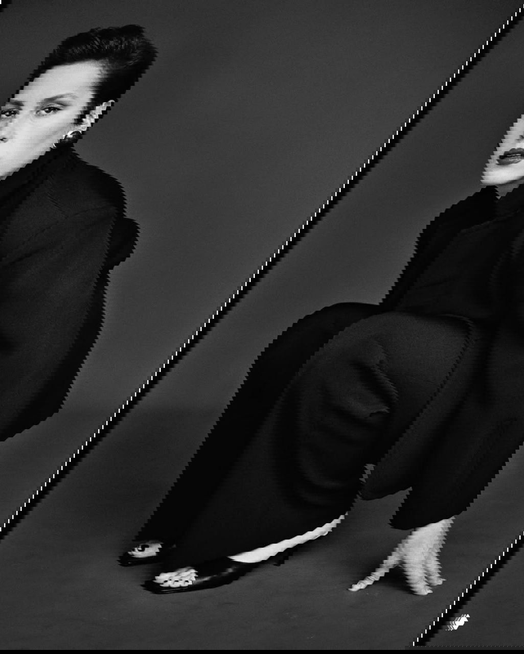 Чёрно‑белая фотография женщины в костюме, драматичная поза и строгая стилистика съёмки, акцент на силуэте и образе.