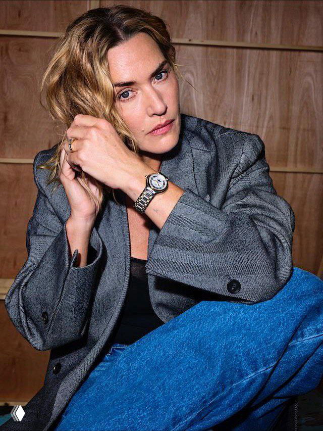 Кадр в пиджаке и джинсах: женщина в естественной позе на студийном фоне, акцент на текстуре одежды и спокойной палитре.