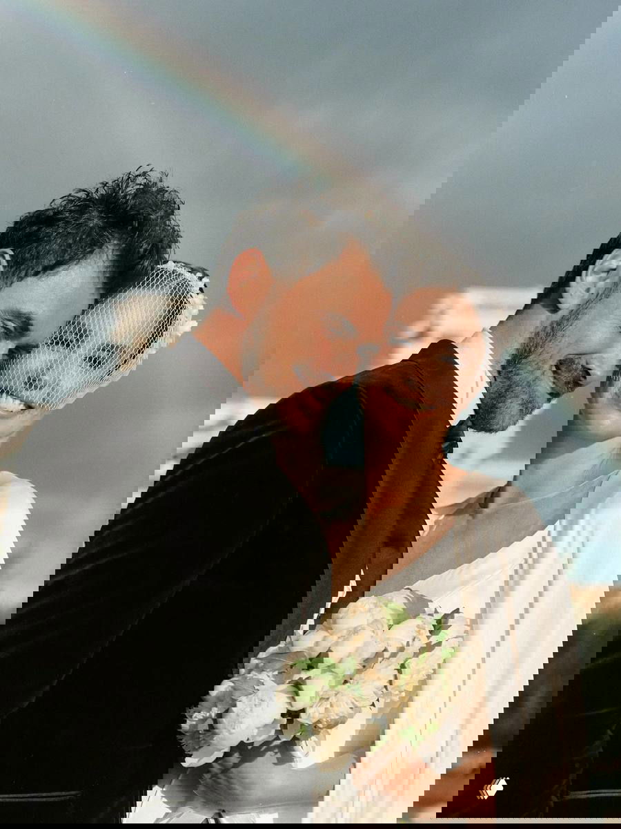 Пётр Дранга обнимает Агату Муцениеце, она держит букет пионов; на заднем плане видна радуга и пасмурное небо