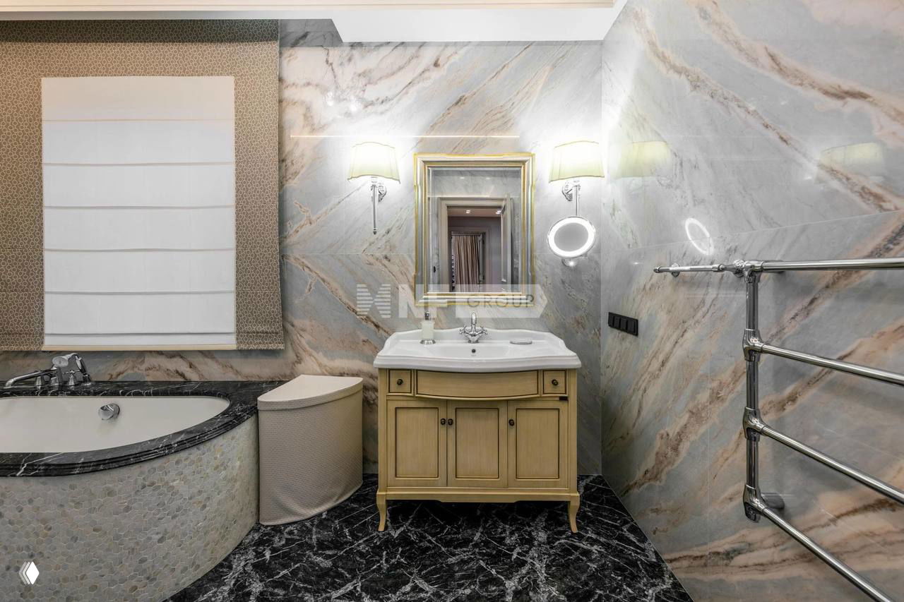 Санузел с мраморной облицовкой и отделкой, раковиной в деревянной тумбе и зеркалом; аккуратная классическая стилистика и тёплое освещение.