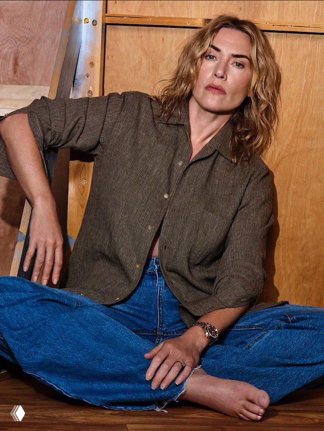 Женщина в рубашке и джинсах, расслабленная поза на полу студии, естественные выражения и тёплая цветовая палитра съёмки.