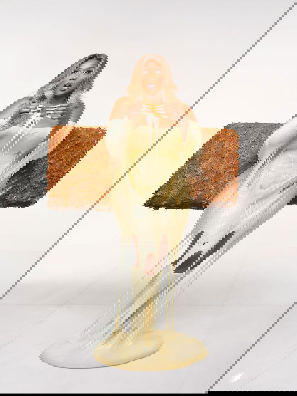 Лиззо в образе палочки моцареллы: пастельный наряд и эффект стекающей моцареллы с крупным едким реквизитом за спиной — юмористическая концепция.