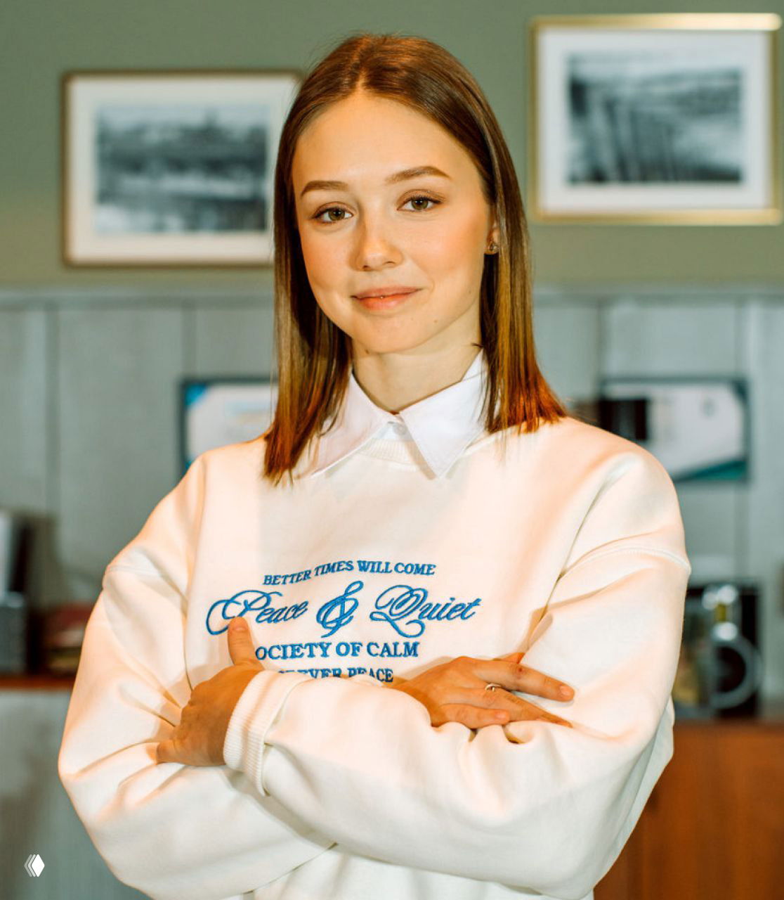 Портрет Екатерины Старшовой в 24 года: актриса в белом свитшоте, мягкий свет, интерьер с рамками на стене, спокойный и уверенный взгляд.