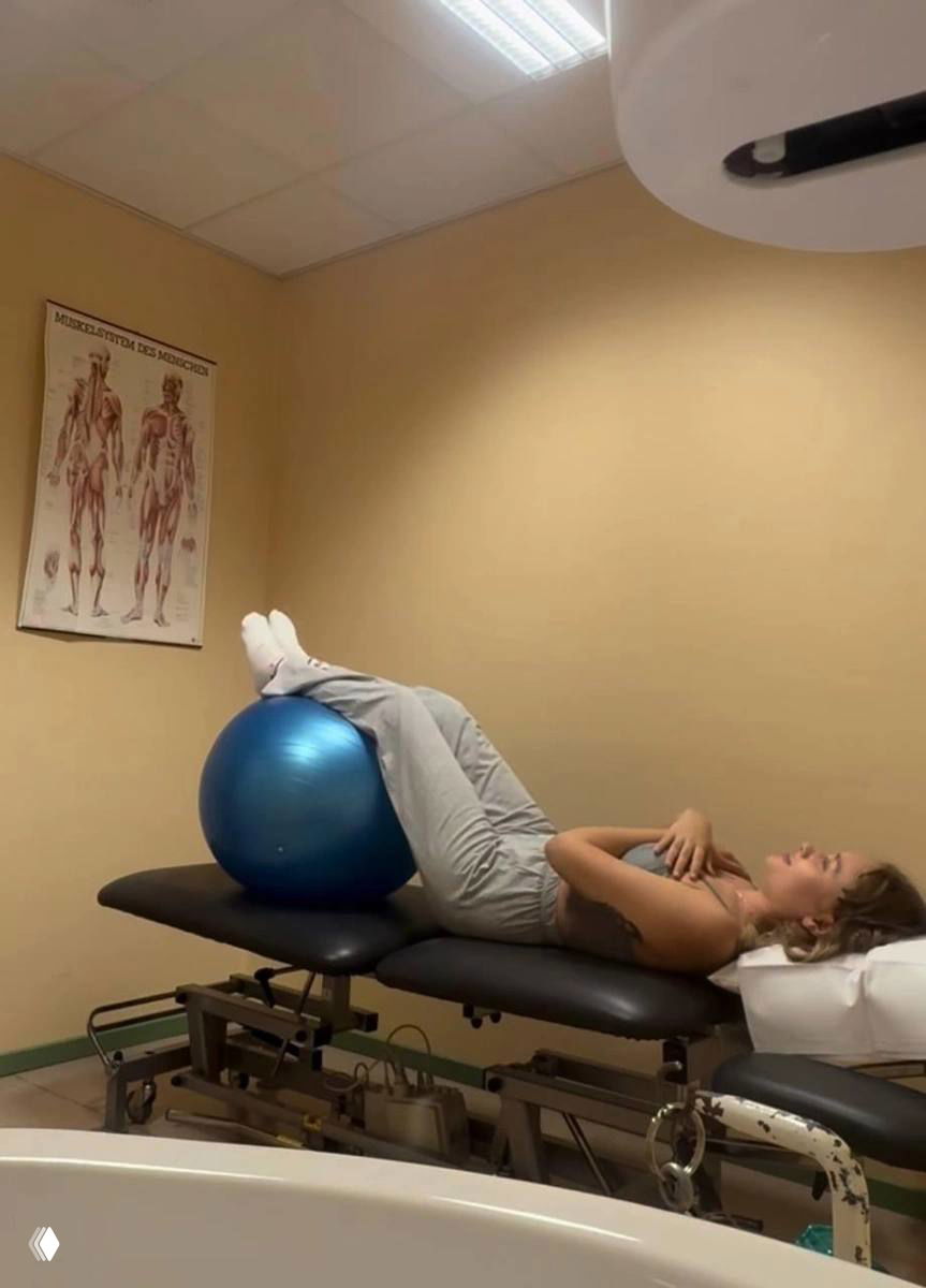 Мария Ковальчук выполняет упражнение с фитнес‑мячом на кушетке в кабинете физиотерапии: лечебная гимнастика и восстановление под контролем специалистов.