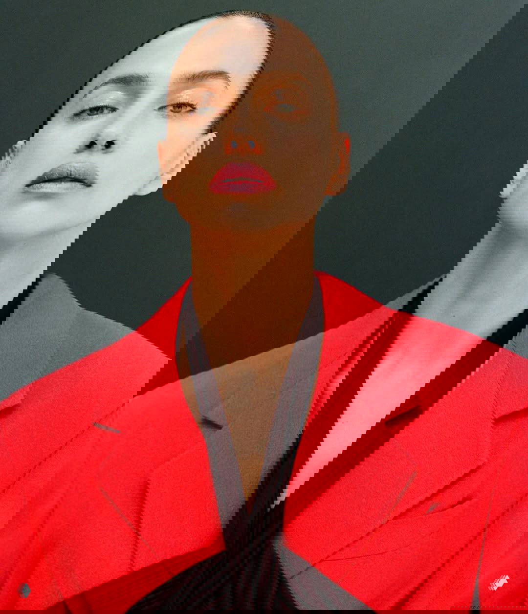 Крупный портрет женщины‑модели в ярком красном пиджаке на нейтральном фоне, строгий макияж и минималистичная fashion‑композиция.