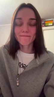 Кадр из вертикального видео: молодая женщина без макияжа в серой толстовке смотрит в камеру в домашней обстановке, на лице усталое и задумчивое выражение.