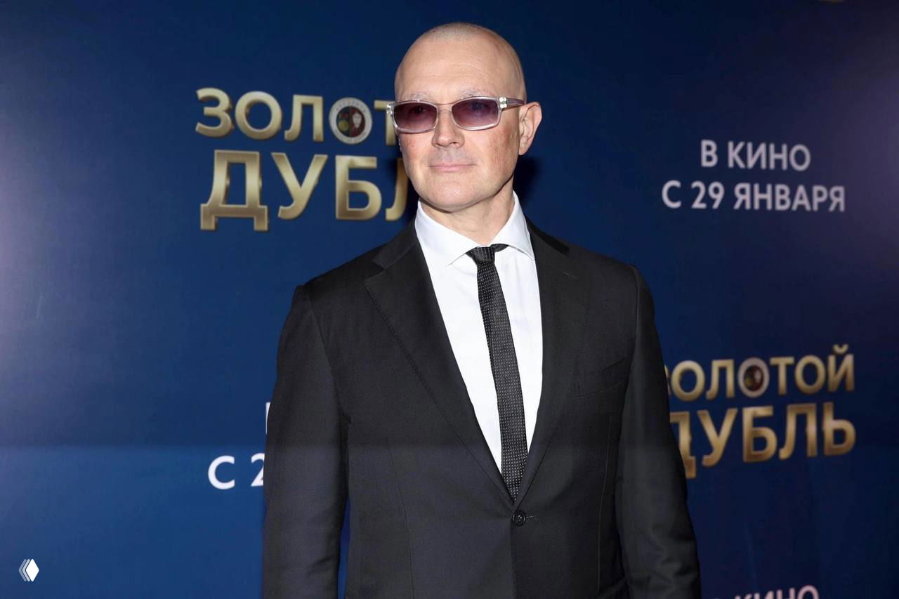 Полноразмерный снимок мужчины в тёмном костюме и солнцезащитных очках с полностью бритой головой на премьере фильма.