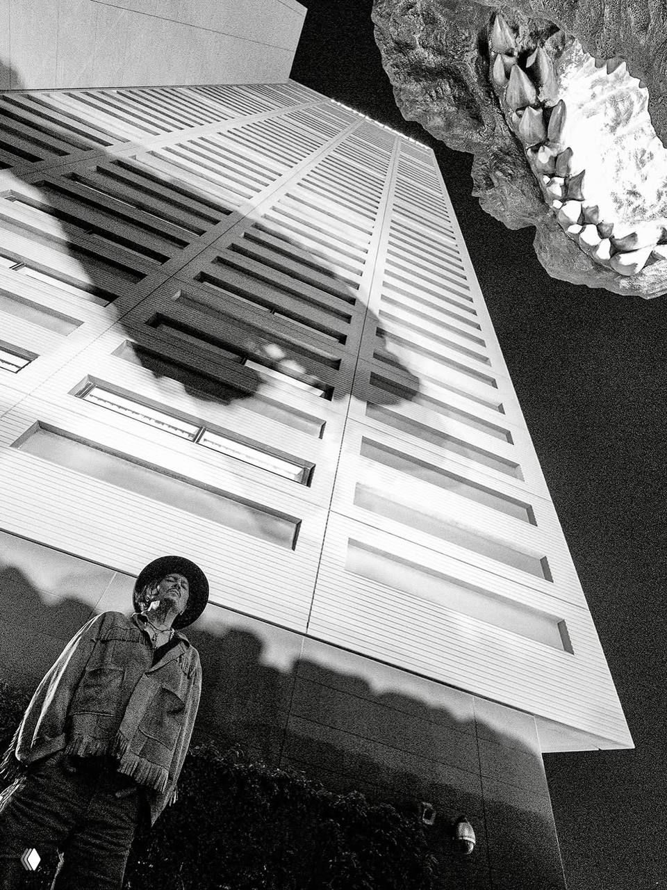 Чёрно-белый снимок с низкого ракурса: мужчина в шляпе на переднем плане, высокая офисная башня и большая скульптура создают драматичный контраст теней в городском пейзаже