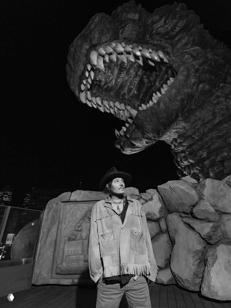 Крупный план раскрытой пасти массивной скульптуры-монстра и силуэт мужчины в шляпе внизу кадра, чёрно-белая драматическая композиция с сильными тенями