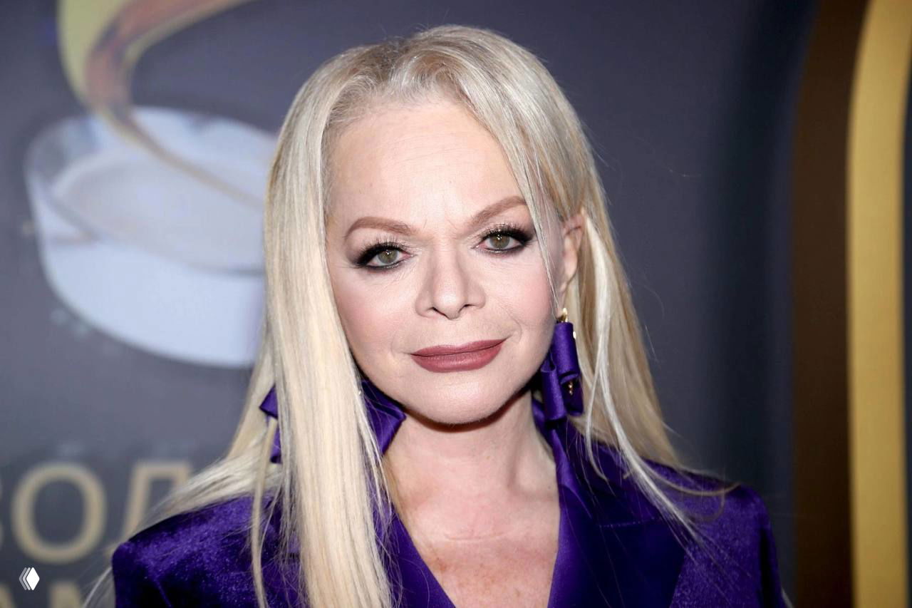 Крупный портрет Ларисы Долиной в фиолетовом костюме на светском мероприятии, выражение лица и макияж, размытый фон.