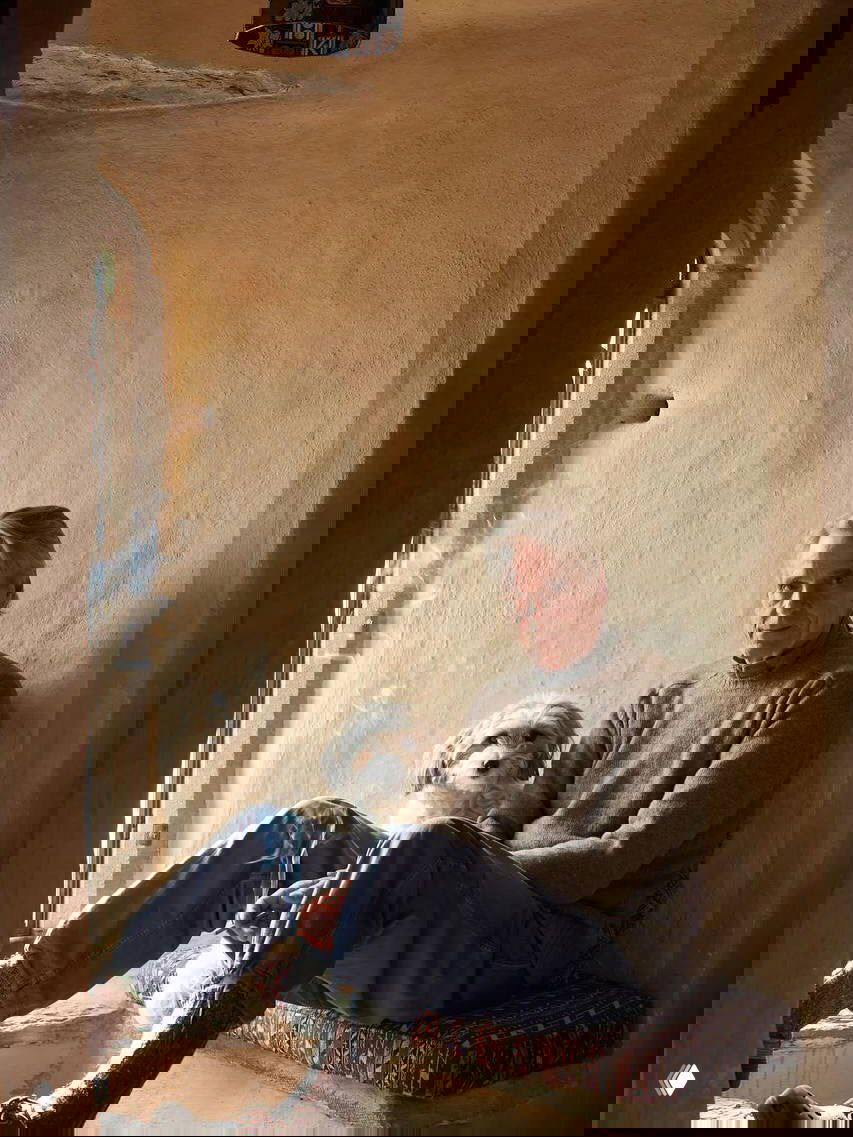 Джереми Айронс сидит у узкого каменного окна в интерьере замка Килко XV века, рядом небольшой собачий компаньон и мягкий рассеянный свет.