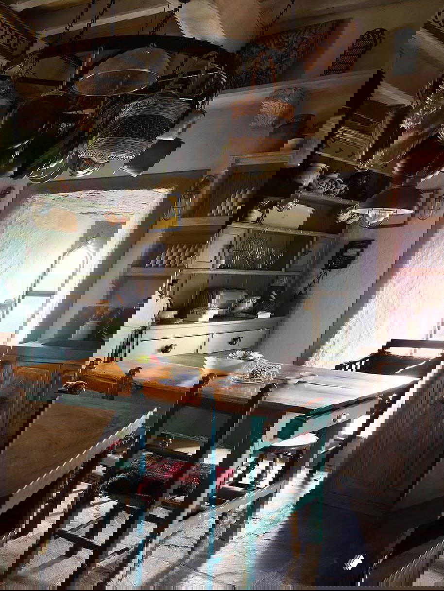 Кухонная зона в замке Килко с массивным деревянным столом, висящими над ним кастрюлями и богато текстурированной отделкой стен и мебели.