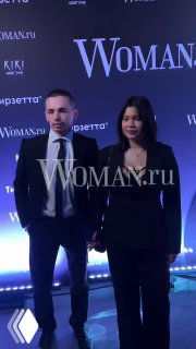 Полина и её спутник Артур в вечерних нарядах позируют на фотозоне Celebrity Party Woman.ru в центре Москвы на фоне логотипа мероприятия.