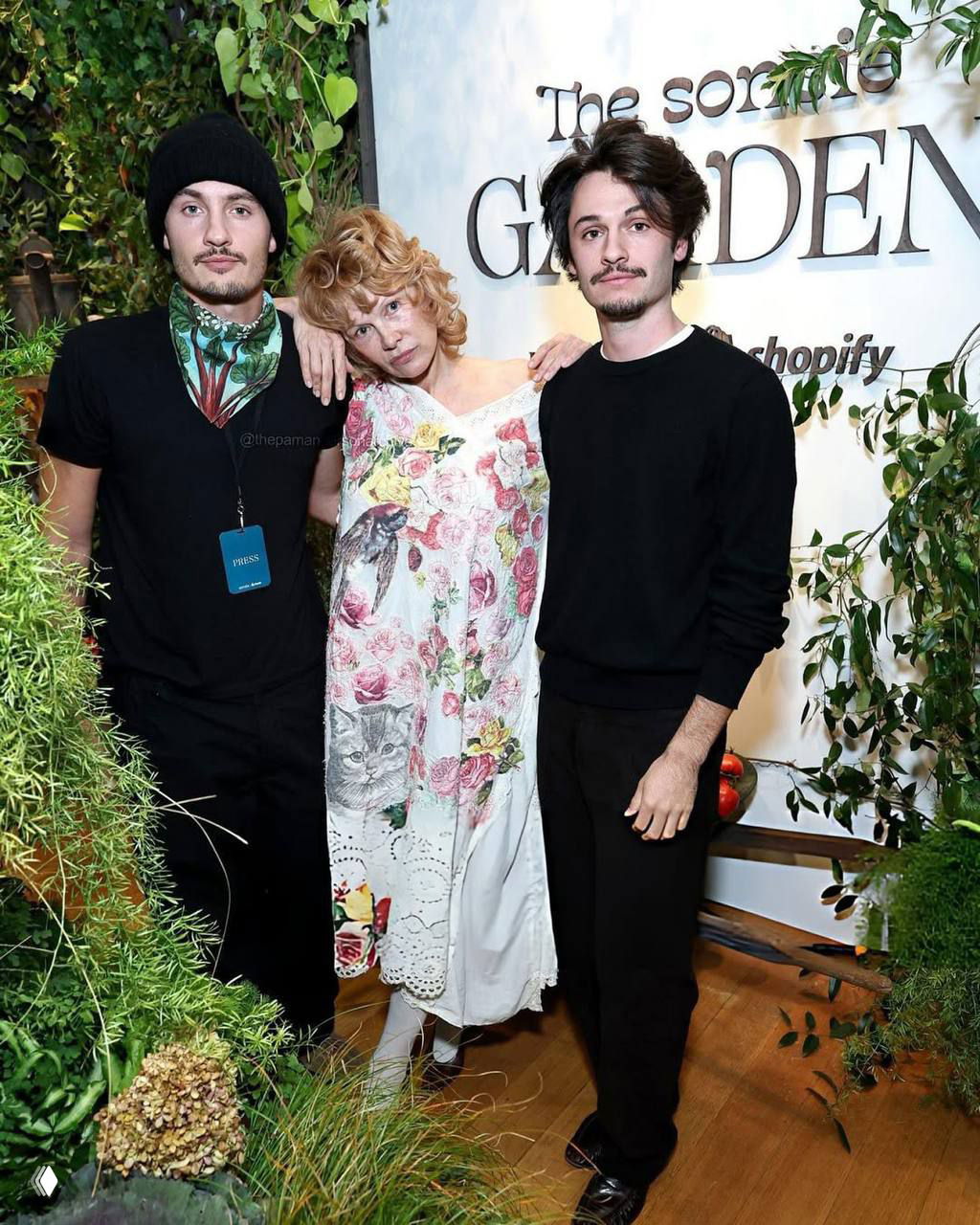 Памела Андерсон в платье с цветочным узором позирует вместе с сыновьями Брэндоном и Диланом у брендового стенда магазина Sonsie.