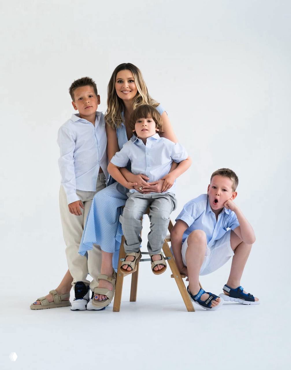 Мама в окружении троих детей на светлом фоне: семейная студийная фотография, дети улыбаются и обнимают мать, атмосфера праздника.