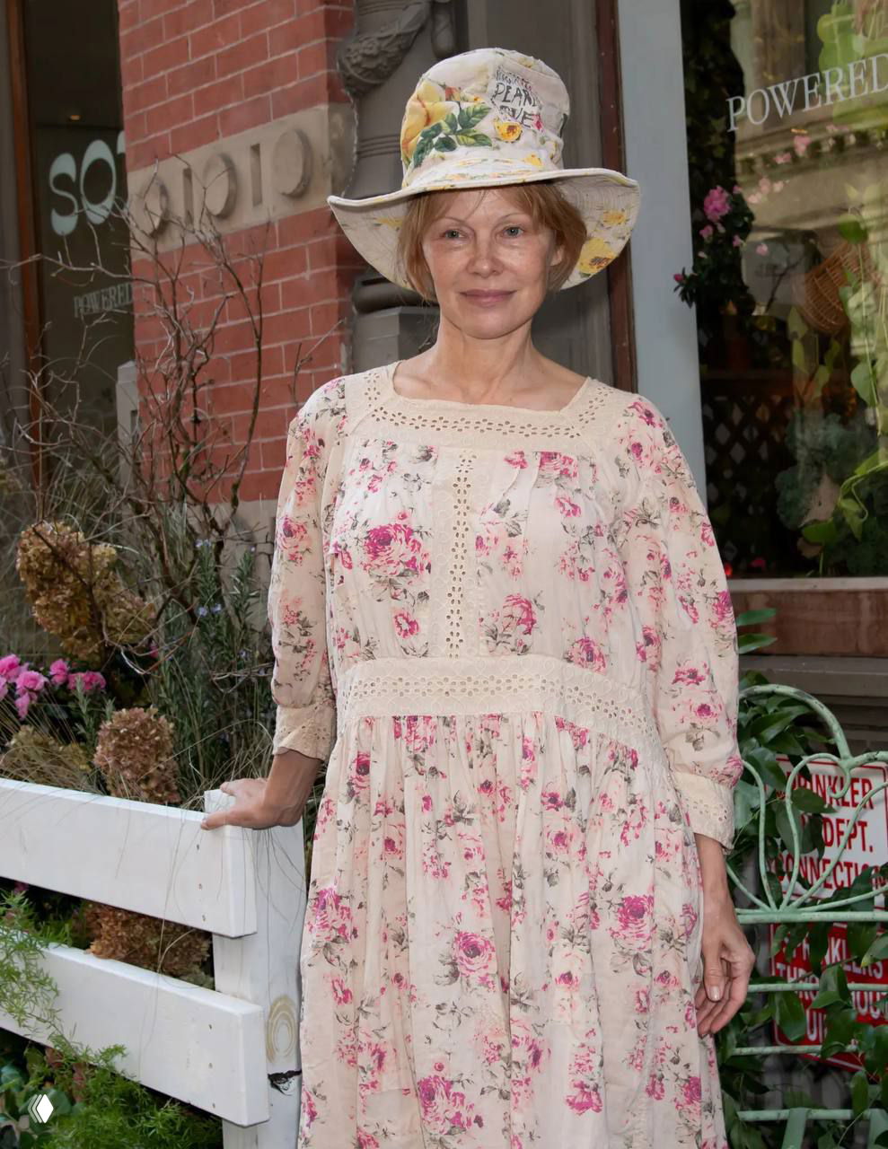 Памела в лёгком платье и широкополой шляпе с цветочным принтом на фоне городского фасада во время мероприятия открытия pop-up магазина.