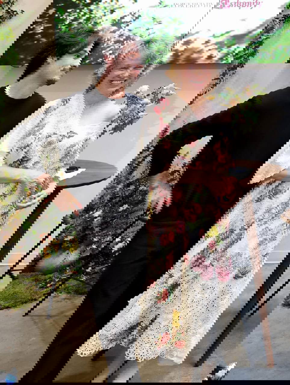 Памела и её сын на презентации косметического бренда, актриса смеётся в длинном платье с крупным цветочным рисунком на фоне интерьера мероприятия.