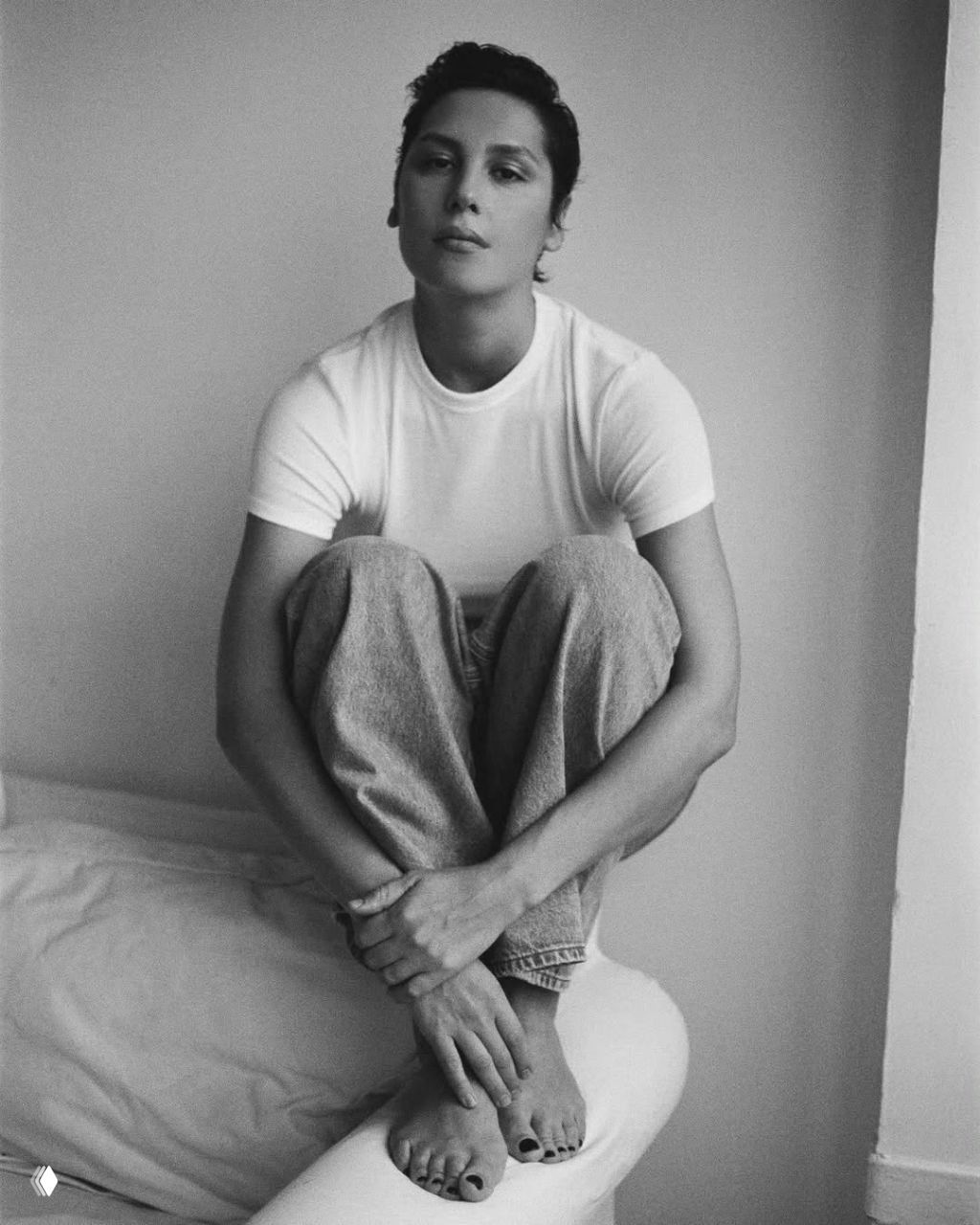 Чёрно‑белое фото: женщина в белой футболке сидит, подтянув колени, минималистичный интерьер и мягкая тональная передача.