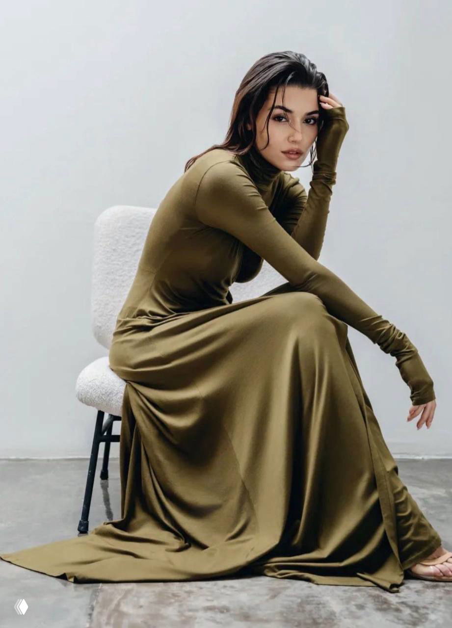 Женщина в длинном оливковом платье сидит на стуле в минималистичном интерьере — изящная и лакончиная композиция снимка.