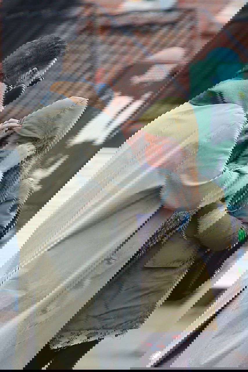 Крупный план: мужчина поправляет капюшон ребёнка в зелёной куртке во время прогулки по улицам города в холодную погоду.