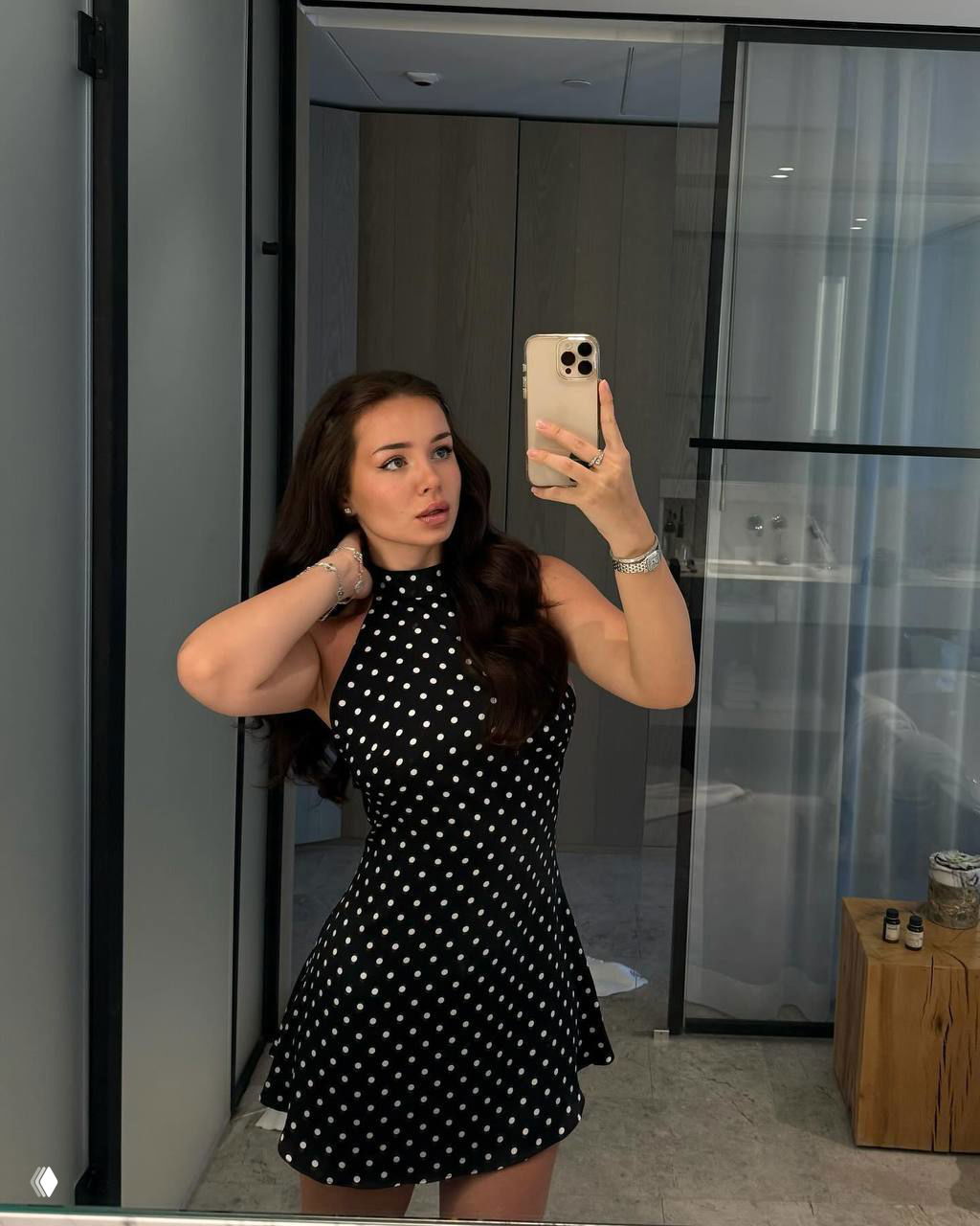 Ника делает селфи в зеркале в чёрном платье в горошек, видна ванная комната и стеклянная перегородка — кадр в домашней обстановке.