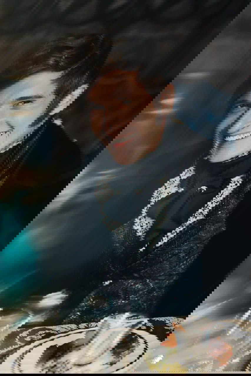 Крупный план Матвея Лыкова в образе Курагина: искренняя улыбка, кружевной жабо и богатая фактура костюма на фоне затемнённого интерьера сцены.