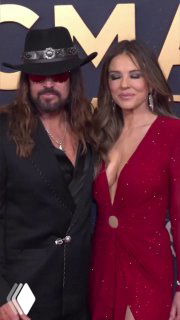 Вертикальное фото пары на красной дорожке: Элизабет и Билли Рэй стоят близко друг к другу, виден общий образ и улыбки — кадр в полноформатном вертикальном формате.