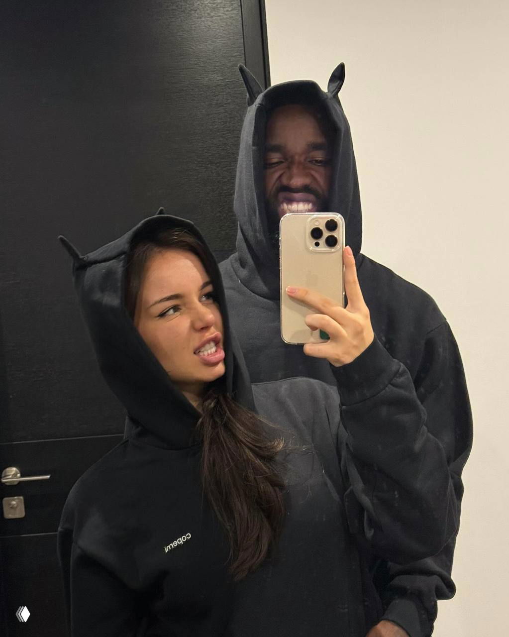 Шутливое селфи пары в одинаковых тёмных толстовках с капюшонами: Ника и мужчина строят гримасы перед зеркалом в квартире.