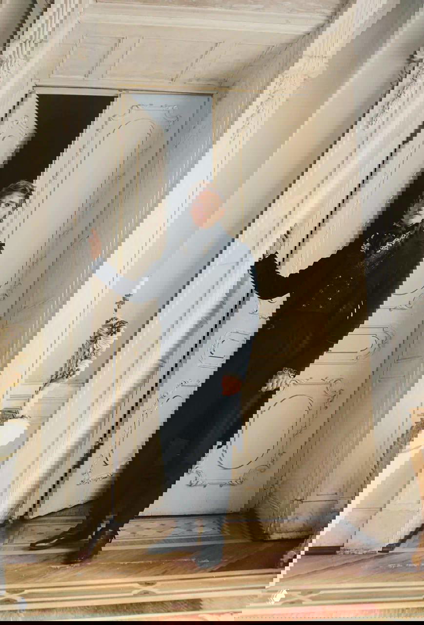 Матвей Лыков в полный рост у декоративной двери дворянского интерьера; полный костюм и поза актёра демонстрируют сценический образ Курагина.