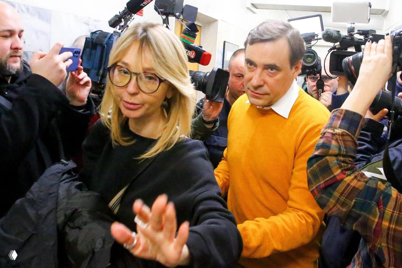 Евгений Цыганов идёт рядом с женщиной в коридоре суда, окружённые фотографами и видеокамерами; активная работа прессы и вспышки.