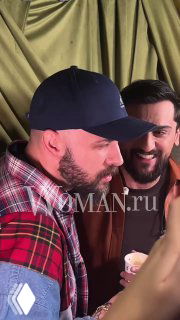 Несколько мужчин беседуют в коридоре презентации; один в бейсболке, другой улыбается на фоне брендового декора мероприятия.